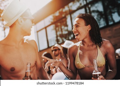 Smiling Couple With Alcoholic Drinks At Poolside. Beautiful Black Woman And Young Man Holding Bottles Of Beer And Having Fun At Poolside. Happy Friends Enoying Pool Party. Summer Vacation Concept