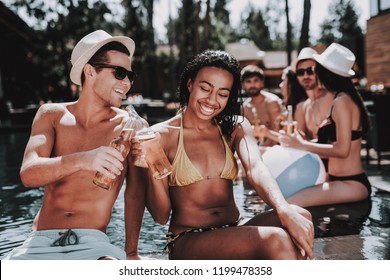 Smiling Couple With Alcoholic Drinks At Poolside. Beautiful Black Woman And Young Man Holding Bottles Of Beer And Having Fun At Poolside. Happy Friends Enoying Pool Party. Summer Vacation Concept