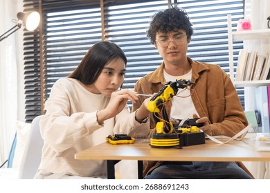 Smiling couple assembling and testing a yellow robotic arm with tools on a table, engaging in a fun DIY tech project indoors.