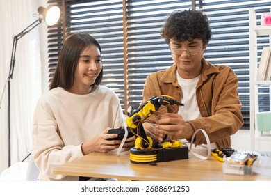 Smiling couple assembling and testing a yellow robotic arm with tools on a table, engaging in a fun DIY tech project indoors.