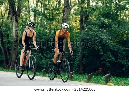 Smiling couple of athletes biking fast on paved road outside of the city. Countryside area, sunny day outdoors. Professional road bicycle racers in action. Concept of endurance and strength.
