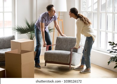 Smiling couple carrying modern chair together placing furniture moving into new home, young family discussing house improvement interior design while furnishing living room, remodeling and renovation