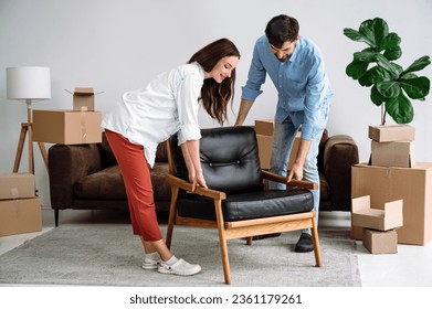 Smiling couple carrying modern chair together, arranging furniture, moving into new flat. Home improvement interior design, furnishing living room, renovation and refurbishment - Shutterstock ID 2361179261
