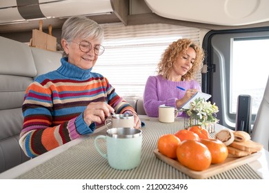 Smiling Couple Of Caucasian Women Multigenerational Family Friends Sitting Inside A Camper Van Motor Home Relaxing With A Herbal The. Lifestyle And Travel Modern People, Vacation Journey Concept