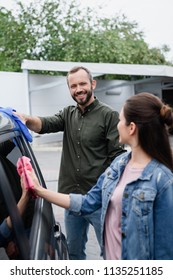 Smiling Couple Cleaning Car With Rags 