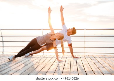 Smiling couple doing yoga exercises outdoors at the beach pier - Powered by Shutterstock