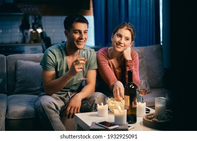 Smiling Couple Drinking Wine And Eating Popcorn While Watching Movie On TV At Night At Home. 