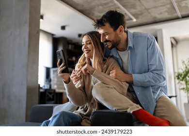 Smiling couple embracing while looking at smartphone. People sharing social media on cellphone. - Powered by Shutterstock