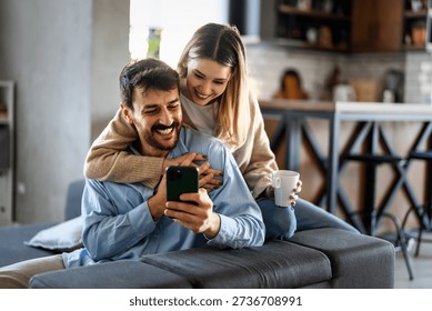 Smiling couple embracing while looking at smartphone. People sharing social media on cellphone.