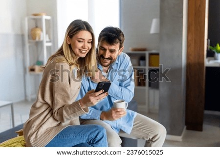 Smiling couple embracing while looking at smartphone. People sharing social media on smart phone.