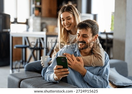 Smiling couple embracing while looking at smartphone. People sharing social media on cellphone.
