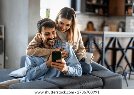 Smiling couple embracing while looking at smartphone. People sharing social media on cellphone.