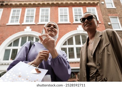 Smiling couple of friends in standing in front of window shop. They are multicultural female friends, one of them is muslim and she is wearing a hijab. The other one is a mixed race woman short hair. - Powered by Shutterstock