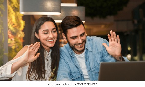 Smiling Couple Of Friends Using Laptop Making Video Call Waving Hands Sitting In Cozy Cafe. Modern Lifestyle And Communication - Powered by Shutterstock