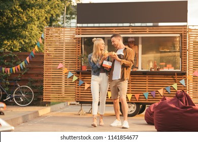 Smiling Couple Holding French Fries And Burger Near Food Truck