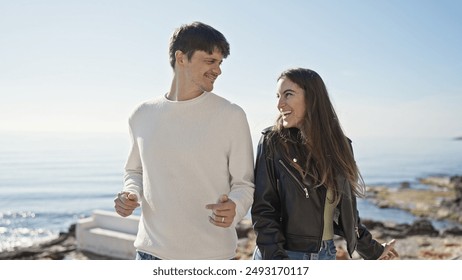 A smiling couple holding hands on a sunny beach promenade with a clear ocean in the background - Powered by Shutterstock