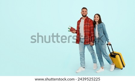 Smiling couple holding tickets and passports walking in studio on blue backdrop, anticipating holiday adventure. Boyfriend and girlfriend posing with travel documents. Panorama, free space