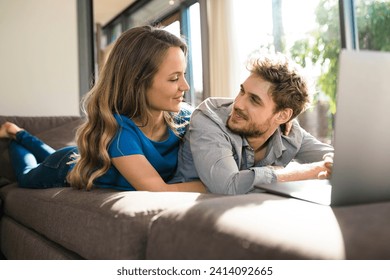 Smiling couple with laptop lying on sofa at home
