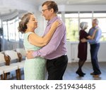 Smiling couple looking at each other while dancing slow dance in modern ballroom