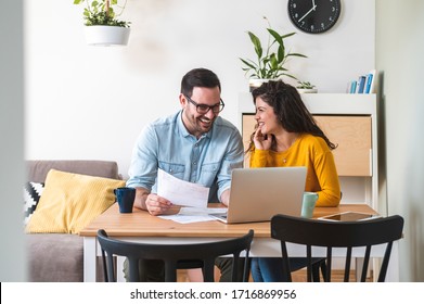 Smiling couple managing finances, reviewing their bank accounts using laptop computer and calculator at modern kitchen stock photo