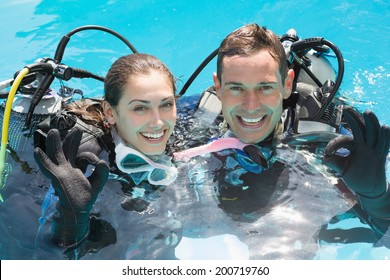 Smiling couple on scuba training in swimming pool showing ok gesture on a sunny day - Powered by Shutterstock