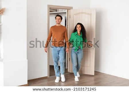 Smiling couple opening door and walking in their apartment, entering new home, happy cheerful young guy and lady standing in doorway of modern flat, looking at design interior together, coming inside