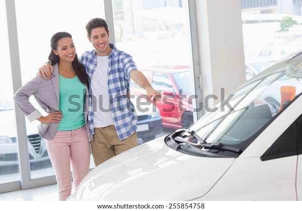 Smiling couple\
pointing a car at new car\
showroom