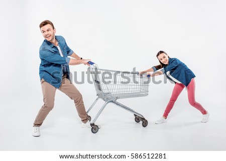 smiling couple pulling empty shopping cart and looking away isolated on white