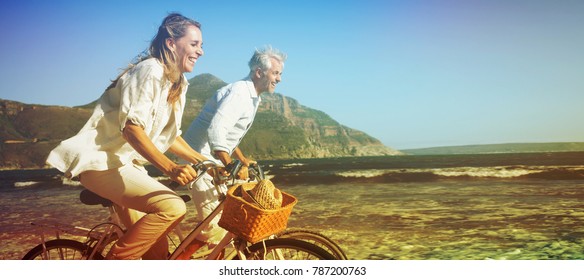 Smiling Couple Riding Their Bikes On The Beach On A Sunny Day