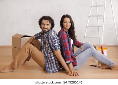 Smiling couple sitting back-to-back on the floor, taking a break during a DIY home renovation project. Ideal for concepts related to home improvement, interior design, and project collaboration.  - Powered by Shutterstock