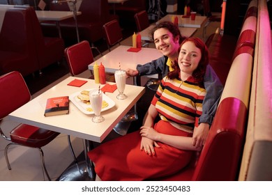 Smiling couple sitting closely in classic retro diner booth enjoying milkshakes and meal, books placed nearby on the table. Decor with red and white upholstery creating vibrant atmosphere - Powered by Shutterstock