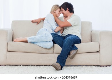 A Smiling Couple Are Sitting On A Couch Looking At Each Other With Their Heads Held Close Together