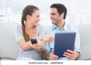 Smiling Couple Sitting On The Couch Using Tablet Pc And Watching Tv At Home In The Living Room