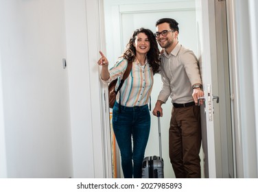 Smiling Couple With Suitcase Arriving In Apartment.