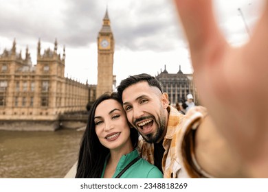 Smiling couple taking selfie portrait during travel in London, England - Young tourist taking vacation photo with iconic England landmark - Happy people wandering around Europe concept - Powered by Shutterstock