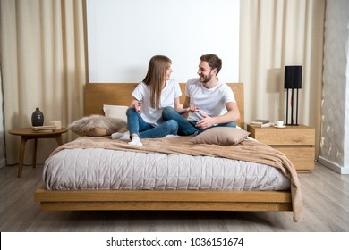 Smiling Couple Talking And Sitting On Bed In Cozy Modern Bedroom