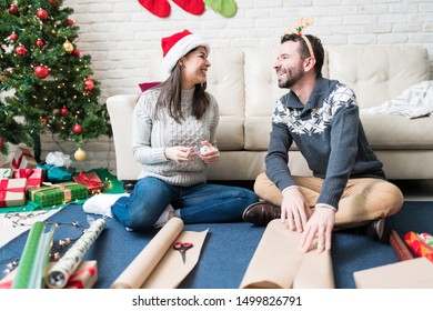 Smiling couple talking while wrapping presents at home during festive season - Powered by Shutterstock