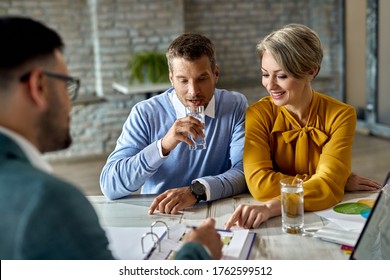 Lächelndes Ehepaar und ihr Immobilienmakler analysieren Entwürfe auf einem Treffen im Büro.