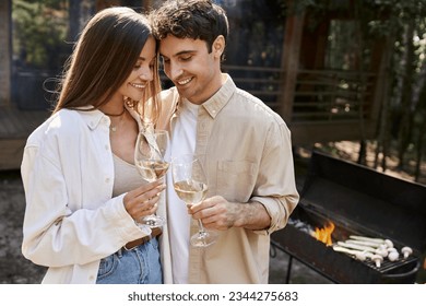 Smiling couple toasting with wine near blurred grill and vacation house at background outdoors - Powered by Shutterstock