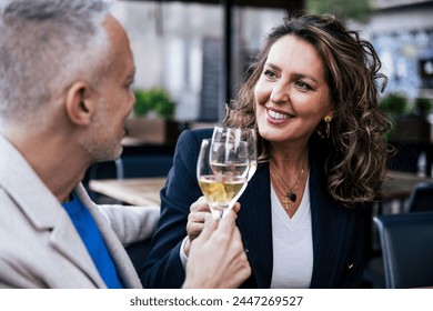 Smiling couple toasting with wine while sitting in a restaurant. Happy middle age woman and man drinking at a terrace looking each other. - Powered by Shutterstock