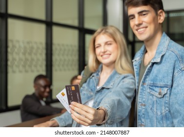 Smiling Couple Travelers In Blue Jeans Paying With Credit Card For Hotel Room Or Airport Lounge. Family Travel Vacation Concept