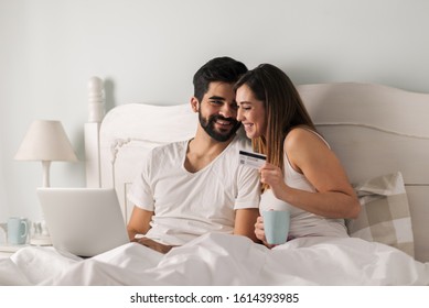 Smiling couple using laptop and credit card for e-commerce while sitting in bed