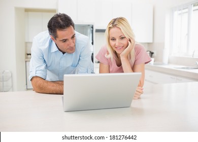 Smiling couple using laptop in the kitchen at home