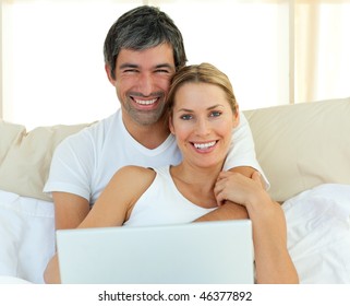 Smiling couple using a laptop lying in the bed at home