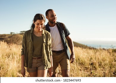 Smiling couple walking together down a hillock enjoying the nature. Couple on a hiking trip on a sunny day.