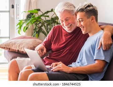 Smiling Couple Of White-haired Grandfather And Teenage Grandson Enjoying Surfing The Net With Laptop. Young And Old Together Share Modernity And Technologies