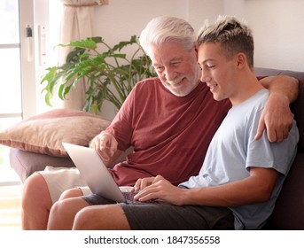 Smiling Couple Of White-haired Grandfather And Teenage Grandson Enjoying Surfing The Net With Laptop. Young And Old Together Share Modernity And Technologies