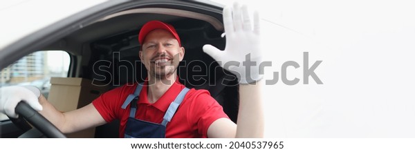 Smiling courier driver in car cab waving his\
hand in greeting