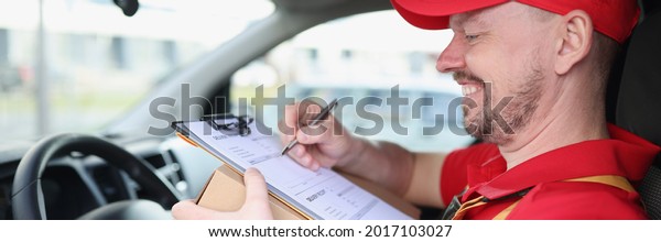 Smiling
courier driver in car with documents and
box