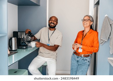 Smiling co-workers sharing a coffee break in the office breakroom, fostering a friendly and relaxed work environment. - Powered by Shutterstock